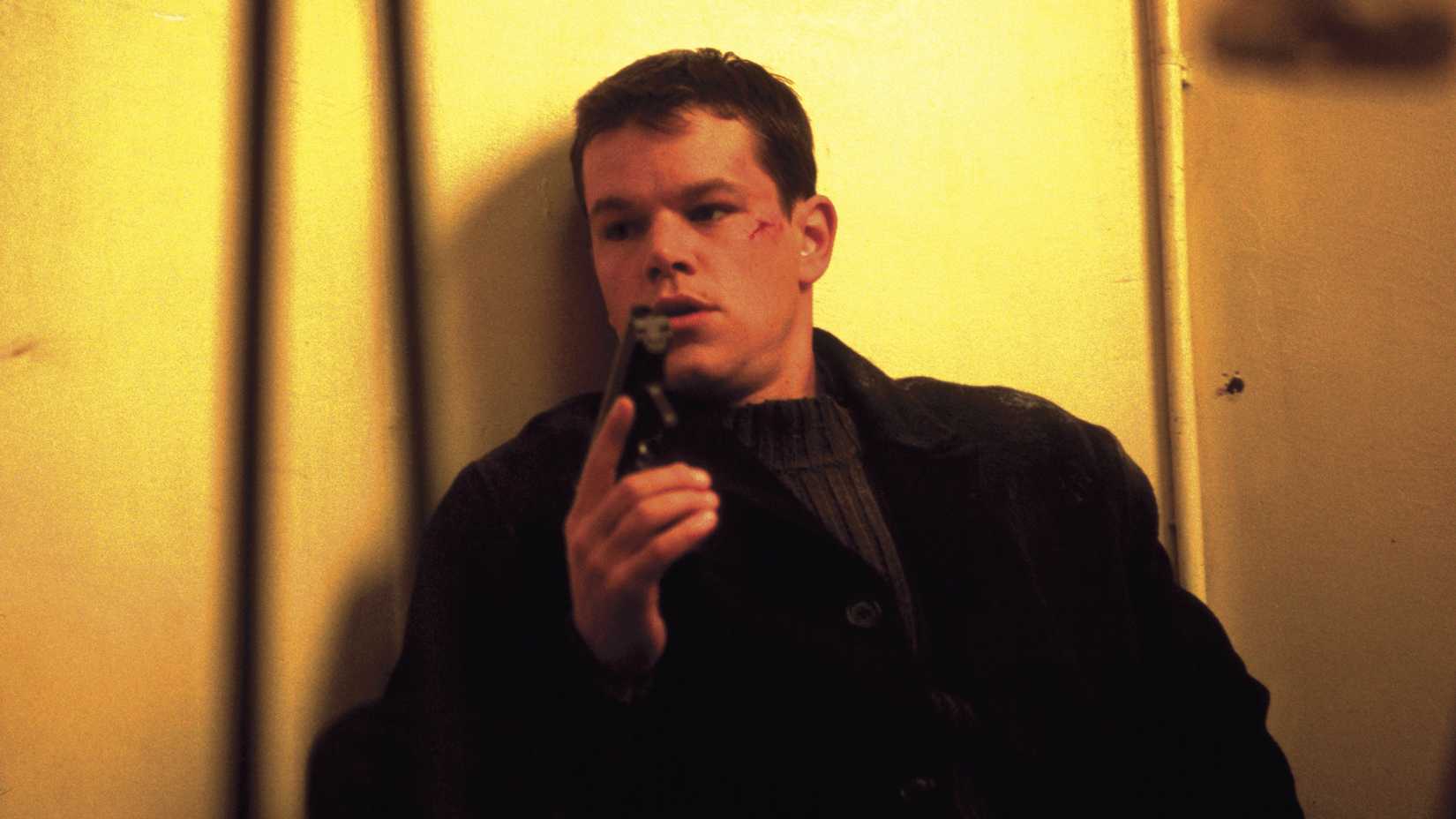 Matt Damon holding a gun with his back faced to a wall in The Bourne Identity