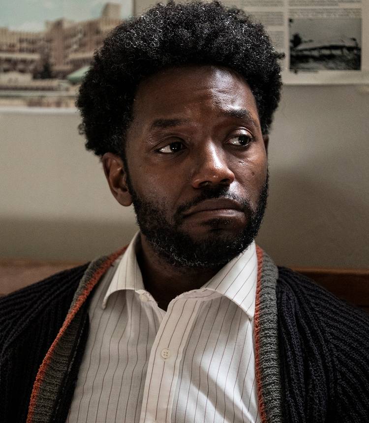 chinaza uche s kofi looking in thought while sitting on his bed in the terror the devil in silver vertical