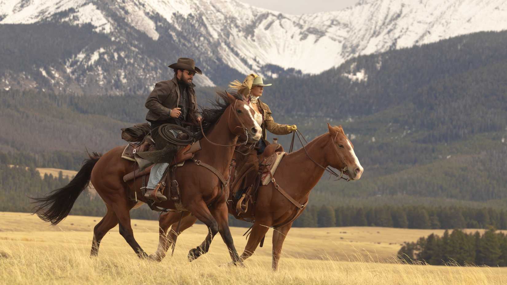 Cole Hauser and Kelly Reilly ride horses fast across a grassy prairie in a scene from Dutton Ranch
