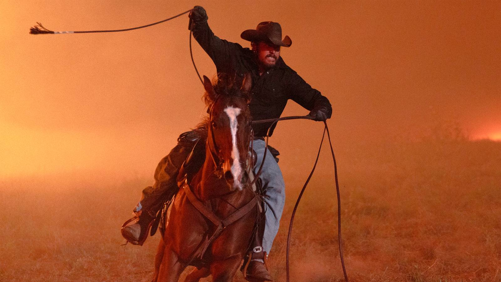 Rip de Cole Hauser mira intensamente mientras monta a caballo y balancea su cuerda en un escenario de fuego en Dutton Ranch.