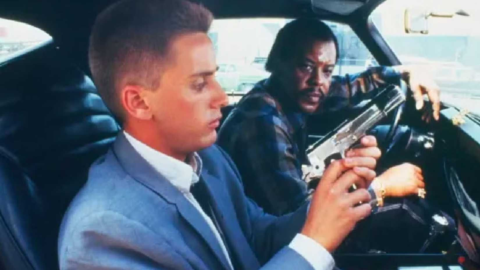 Emilio Estevez as Otto Maddox, loading a gun in a car next to another man in Repo Man