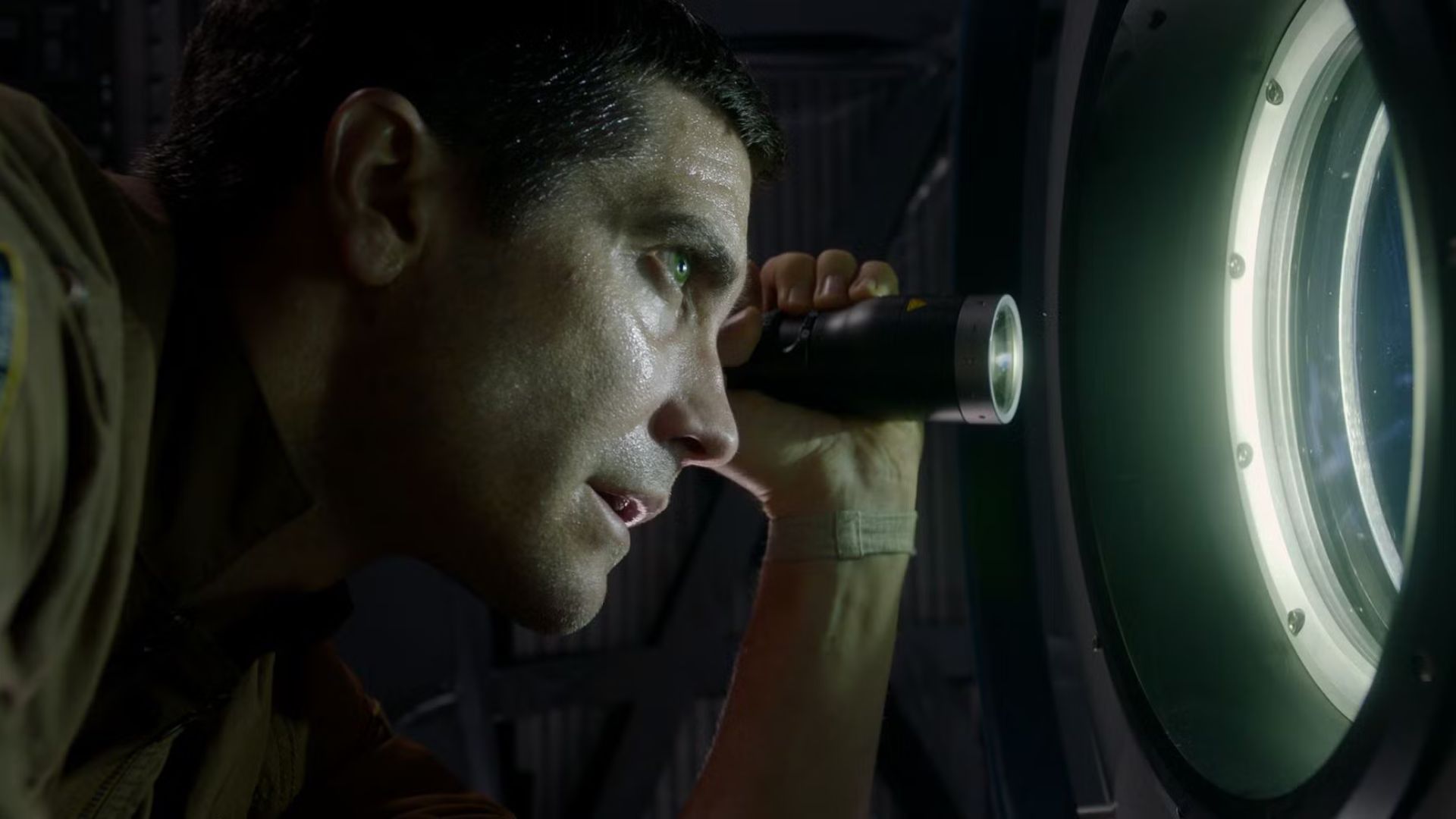 Jake Gyllenhaal shining a flashlight through a window as David Jordan in Life