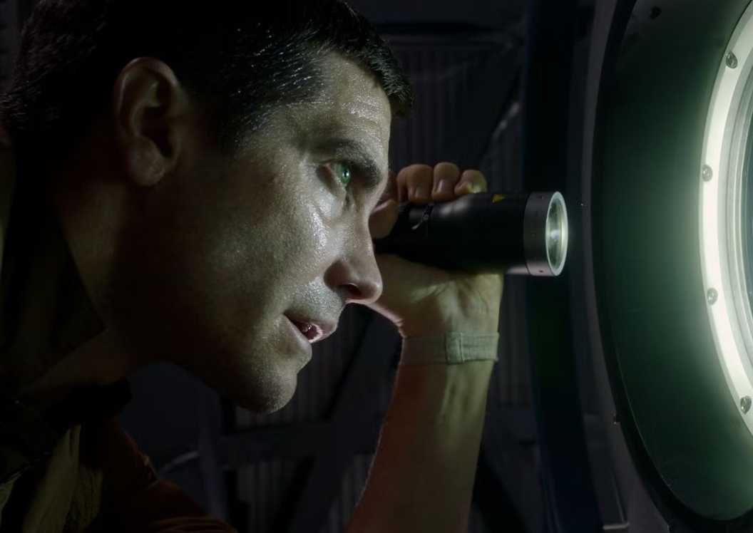 Jake Gyllenhaal shining a flashlight through a window as David Jordan in Life
