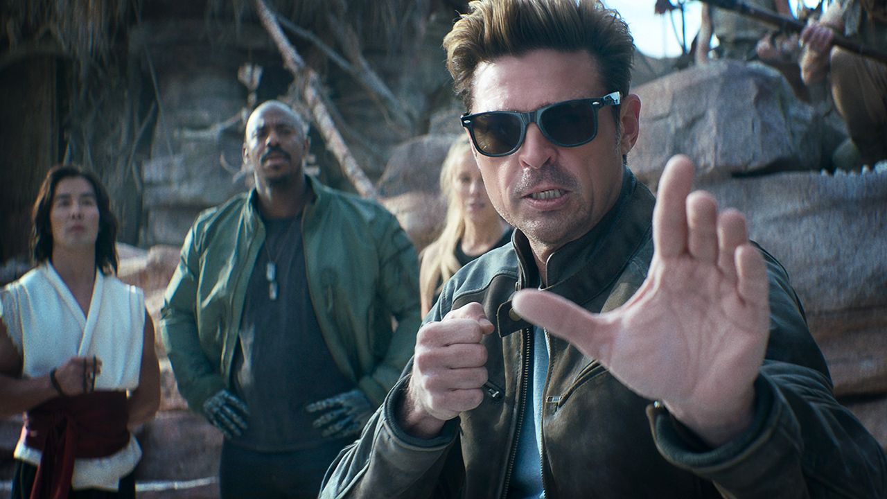 Karl Uban's Johnny Cage looking stern in a fight pose with Ludi Lin's Liu Kang, Mehcad Brooks' Jax and Jessica McNamee's Sonya behind him in Mortal Kombat II