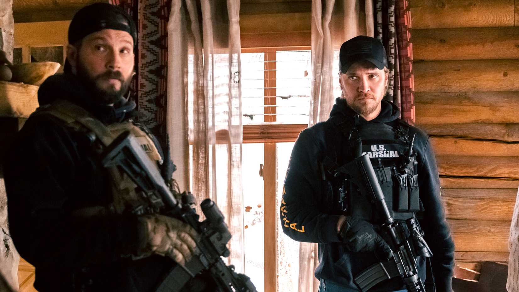 Logan Marshall-Green's Cal and Luke Grimes' Kayce looking intently at someone while holding their rifles in Marshals season 1