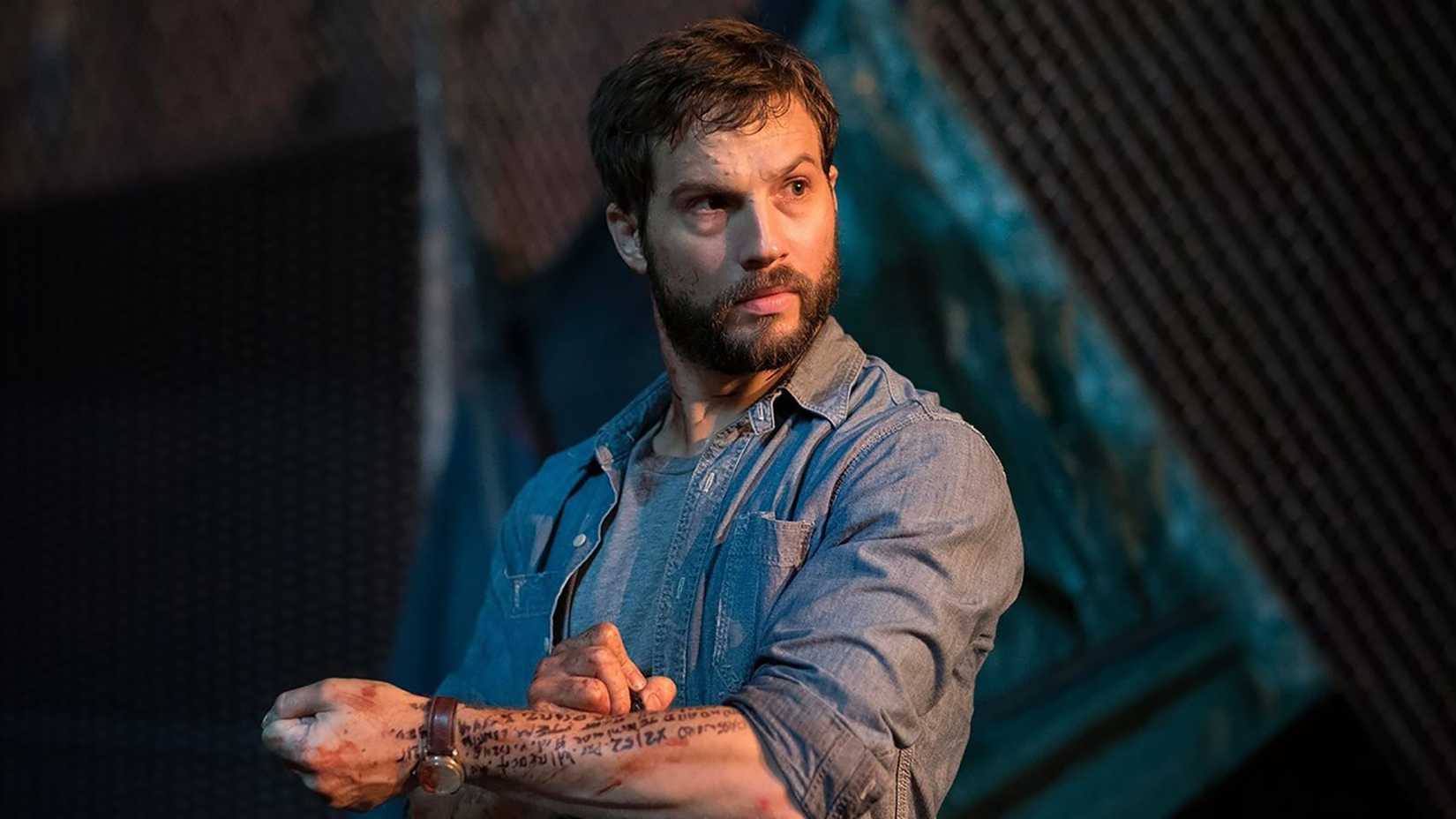 Logan Marshall-Green's Grey looking curiously while writing code on his arm in marker in Upgrade