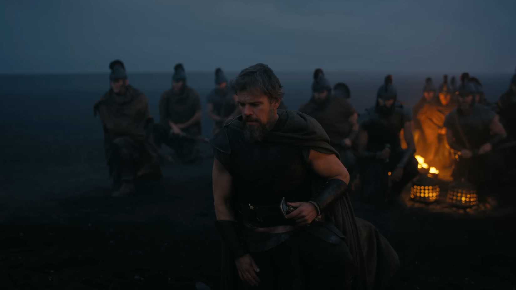 Matt Damon kneels by a fire with warriors by his side in The Odyssey