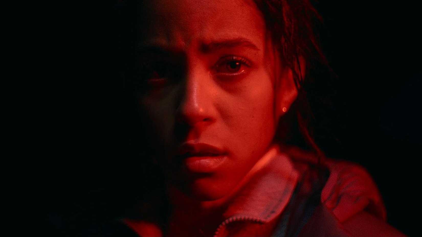 Maddie in close-up lit by red light in Passenger