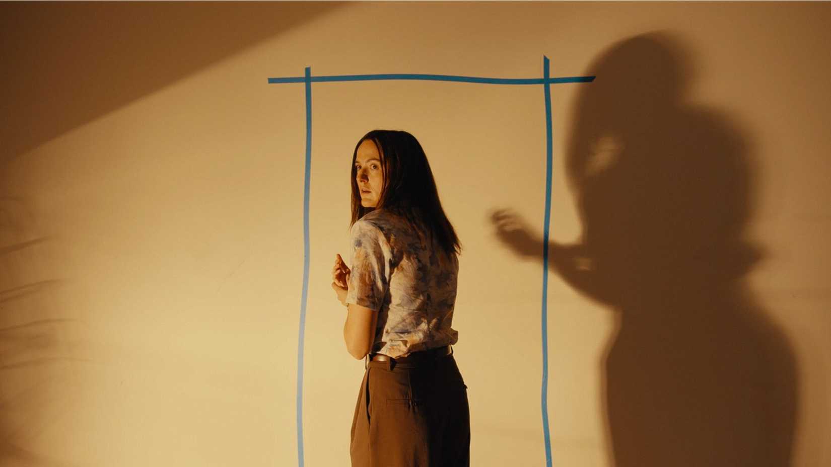 Renate Reinsve standing near an outline of a door with blue electric tape and a lamp in Backrooms