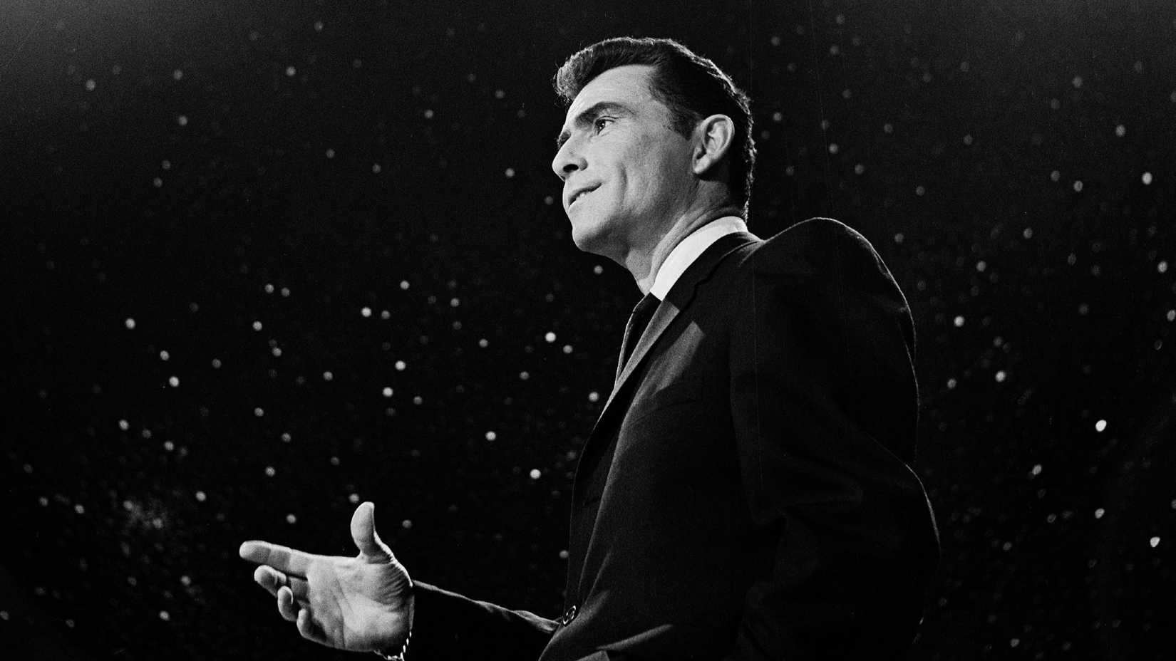 Rod Serling is in front of a black backdrop with stars in The Twilight Zone
