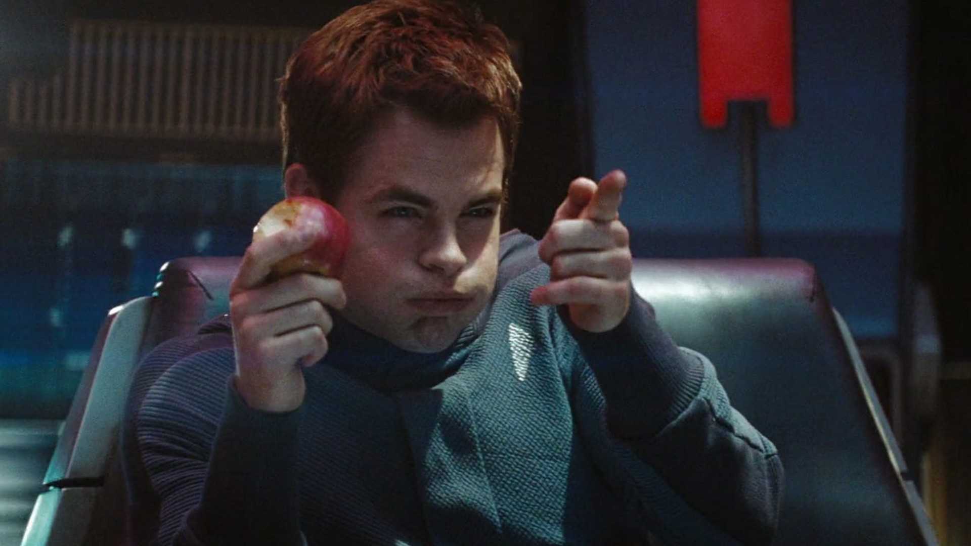 Chris Pine as James Kirk in 2009's Star Trek. He is eating an apple and making a gun with his other hand.