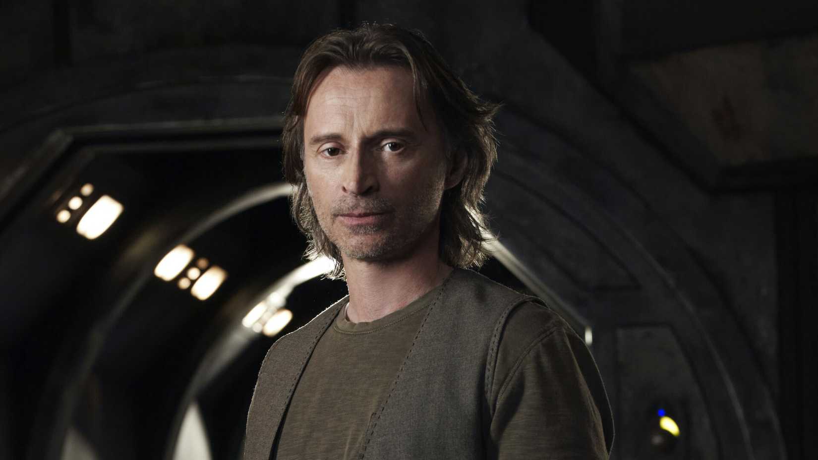 Robert Carlyle standing in dimly-lit spacecraft hallway in Stargate Universe