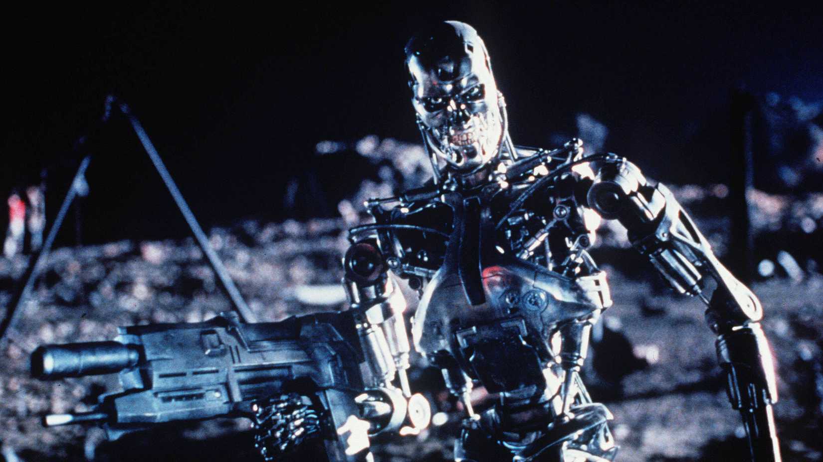 A fully-robotic Terminator holding a machine gun on a post-apocalyptic landscape
