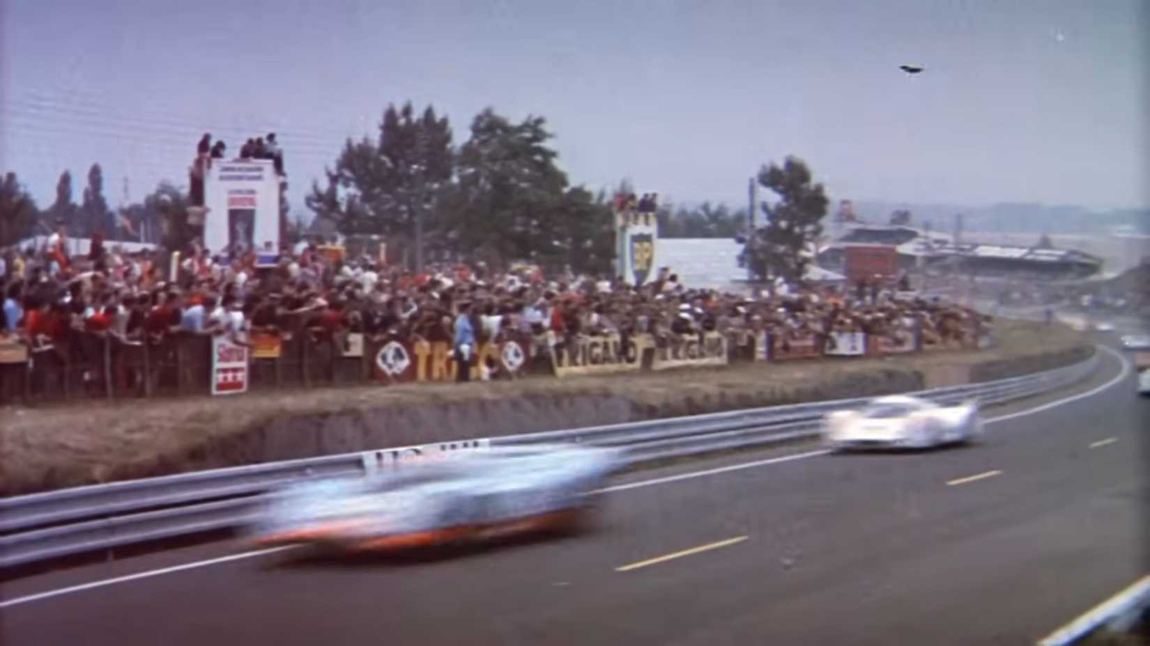 A crowd on the corner of a racing circuit watching cars drive by in Le Mans 1971
