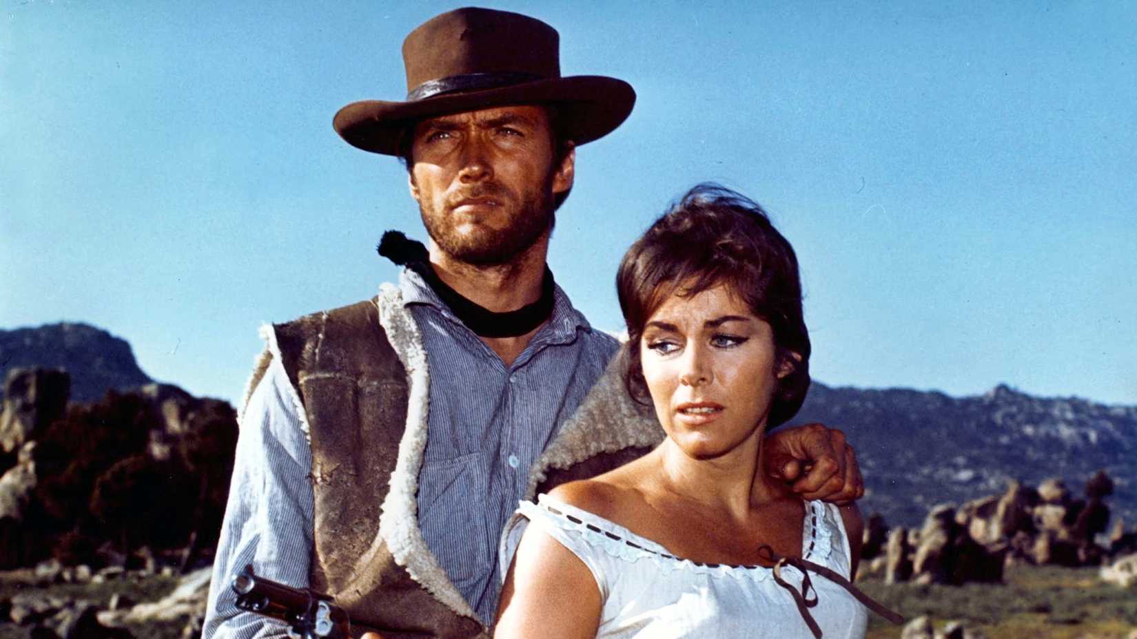 Clint Eastwood stands with his arm around Marianne Koch as they look nervously off camera in A Fistful of Dollars