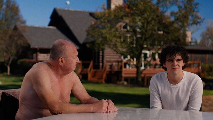 An old, shirtless man sitting with Zeke at a table in Ponderosa