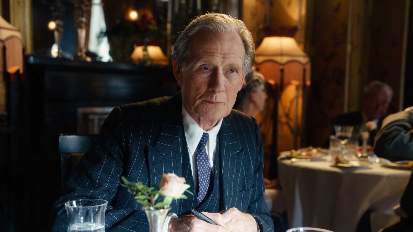 Bill Nighy wearing a suit and sitting at a table in a nice restaurant