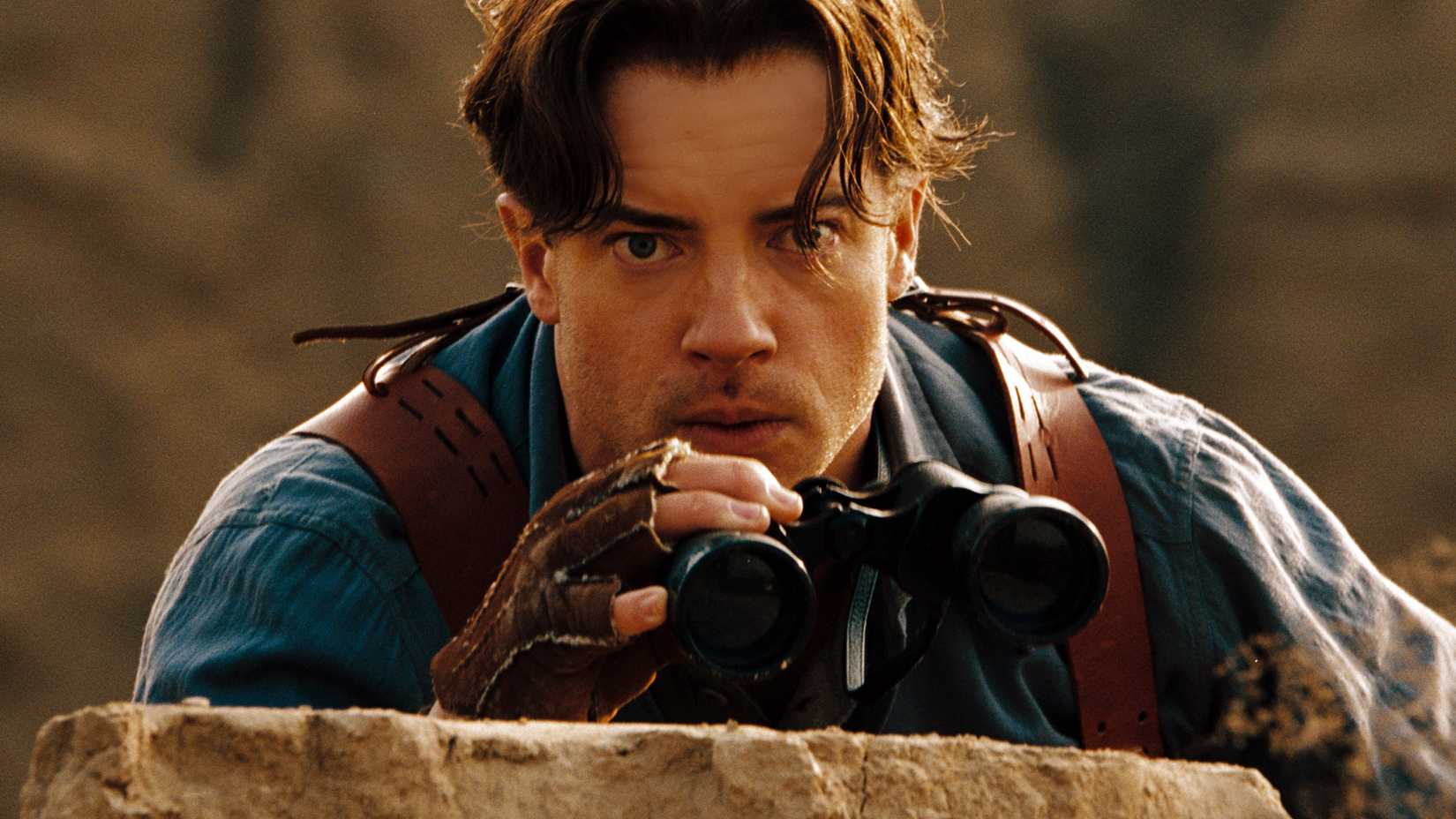Rick O'Connell holding binoculars while peering over the edge of a cliff