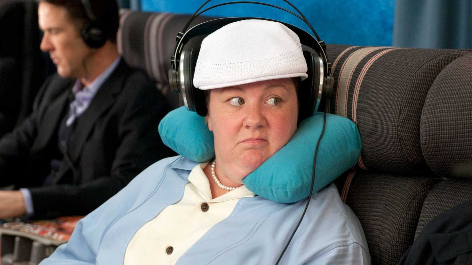 Megan (Melissa McCarthy) on an airplane with a neck pillow and headphones in Bridesmaids.