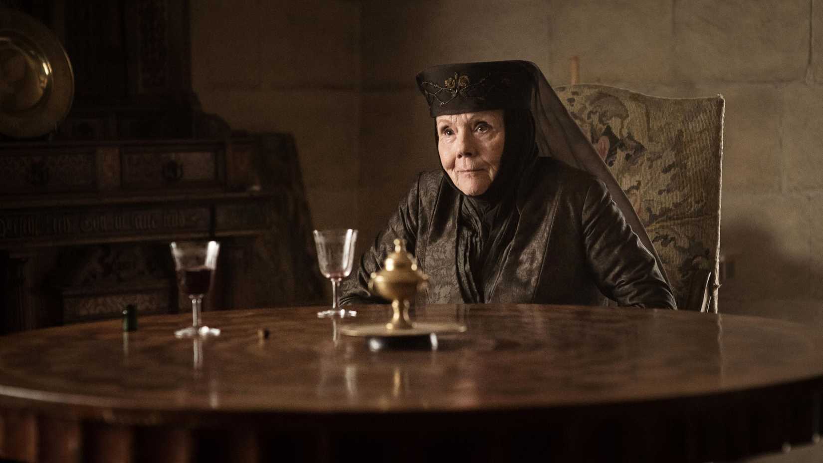 Olenna Tyrell (Diana Rigg) sitting at a table after drinking poison in Game of Thrones.