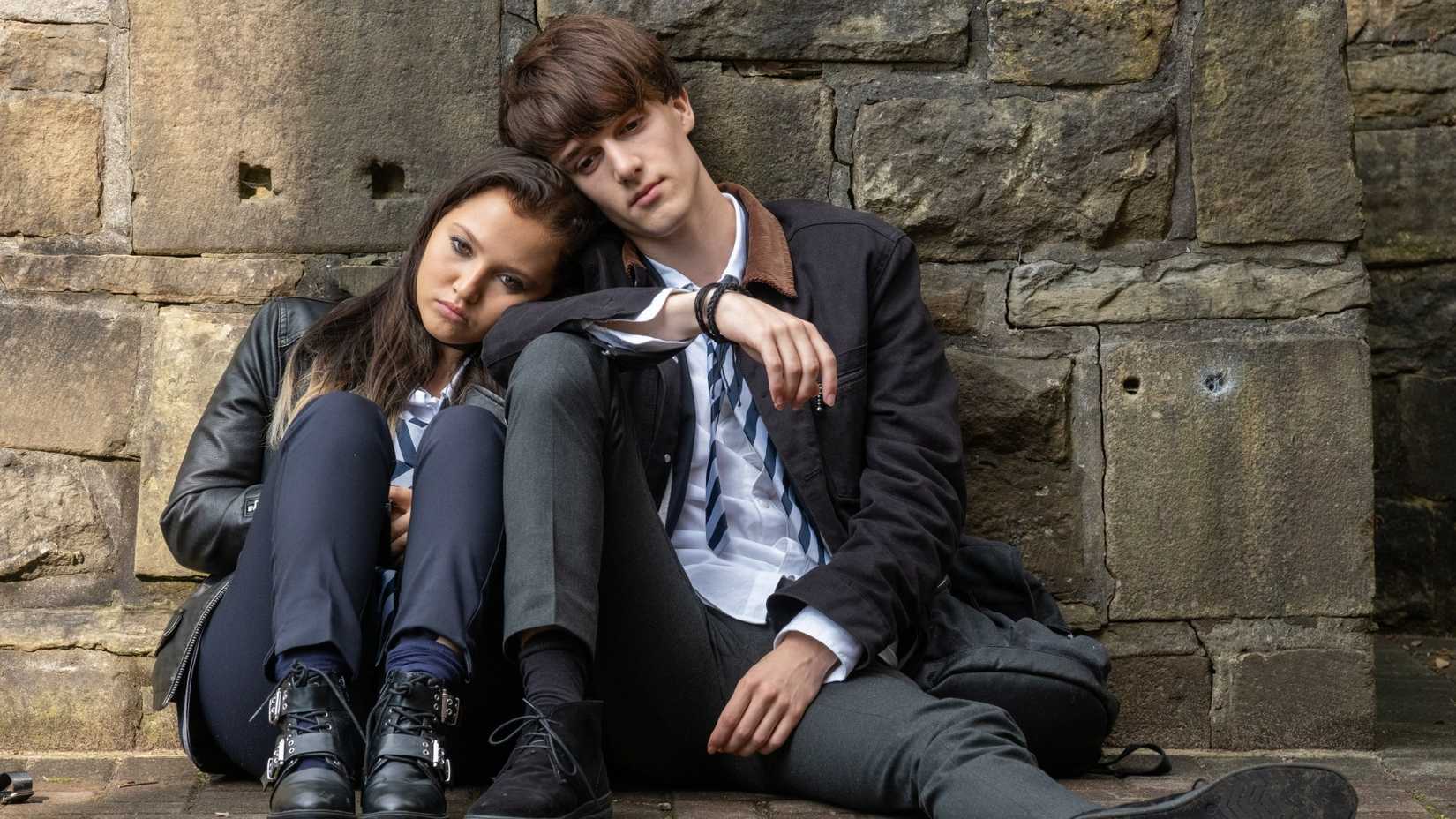 Two teens sit with their heads on each other's shoulders in Get Even