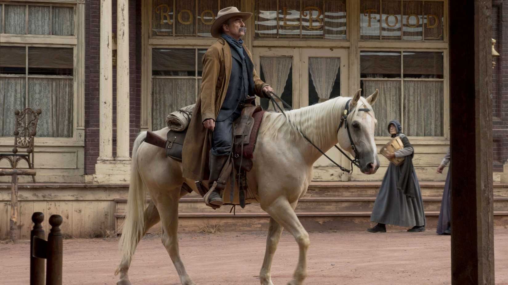 Sam Waterston as Marshall John Cook riding a horse through town in Godless.