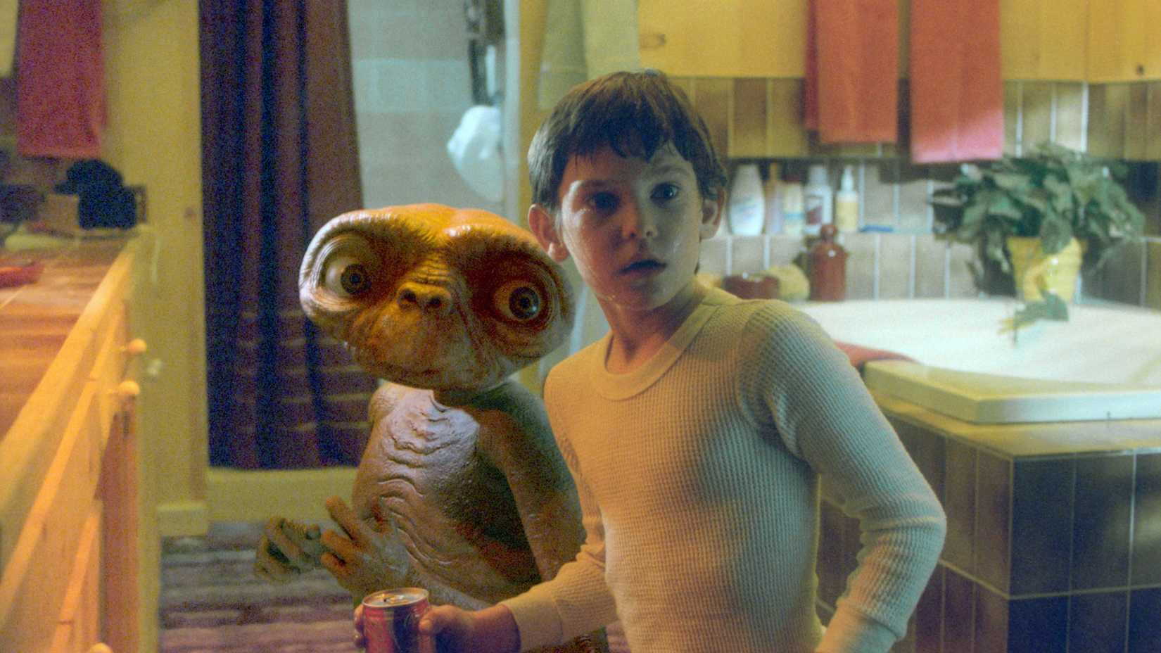 Elliot looking surprised while standing next to E.T. in a kitchen.