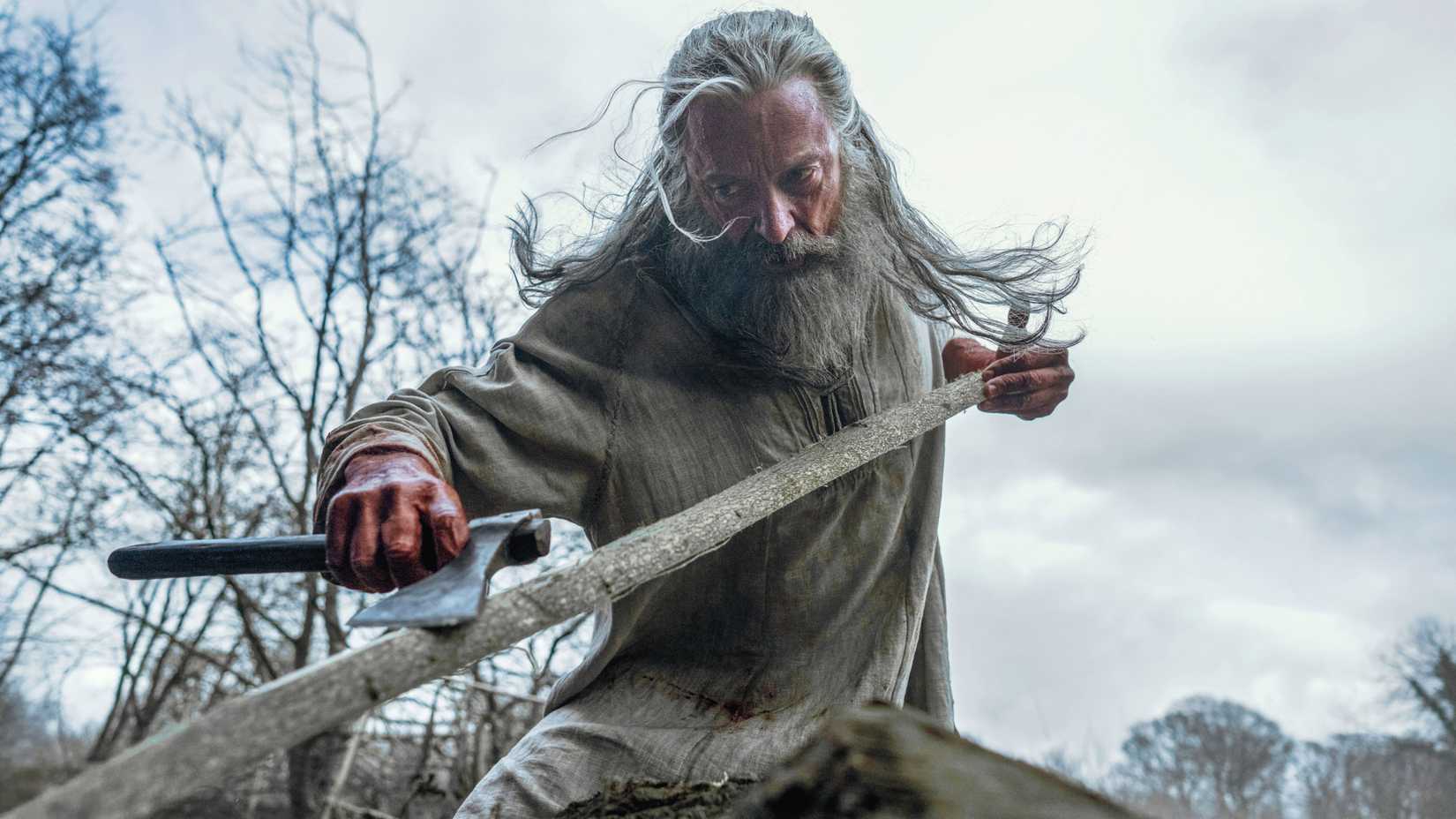 Hugh Jackman's Robin aggressively shaves a tree branch with an ax in The Death of Robin Hood