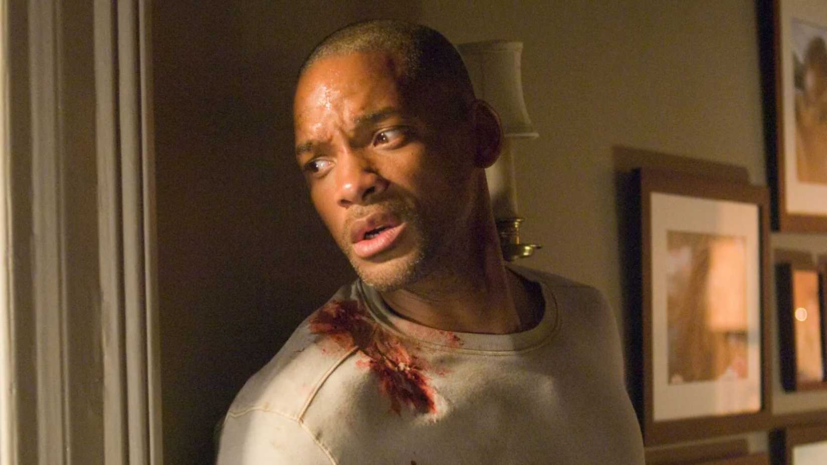 Will Smith looks out a window with a bloodied shoulder in I Am Legend