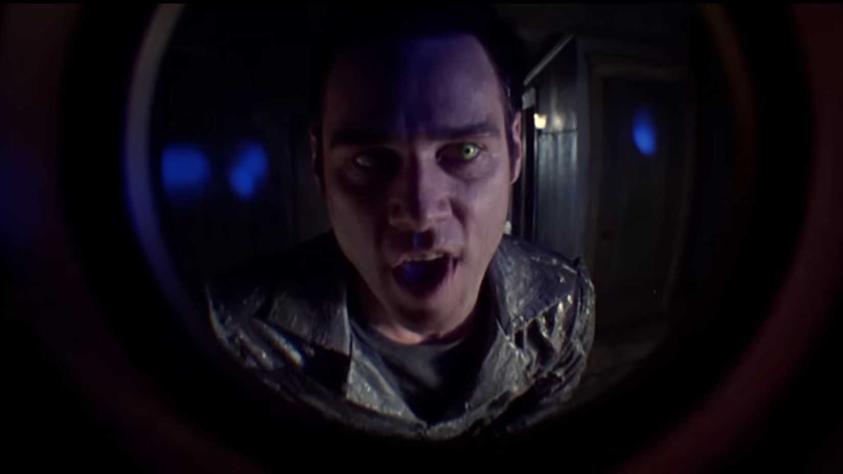 Jim Carrey with scary glowing eyes looking through a peep hole in The Cable Guy