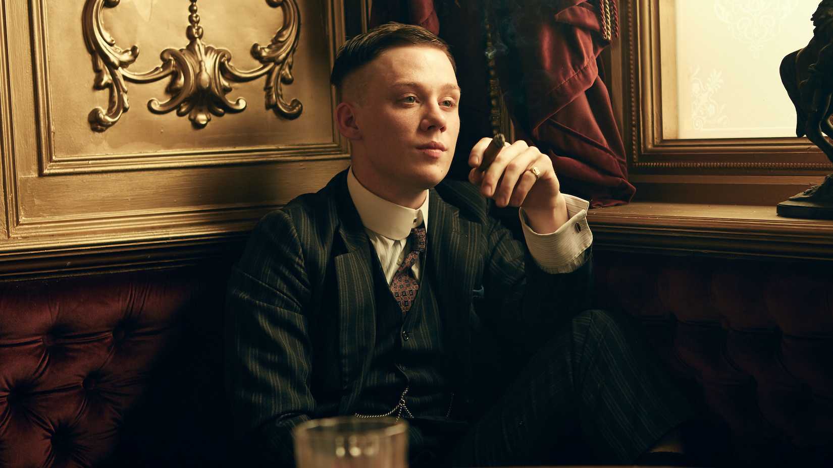 John Shelby holding a cigarette while seated in a restaurant booth