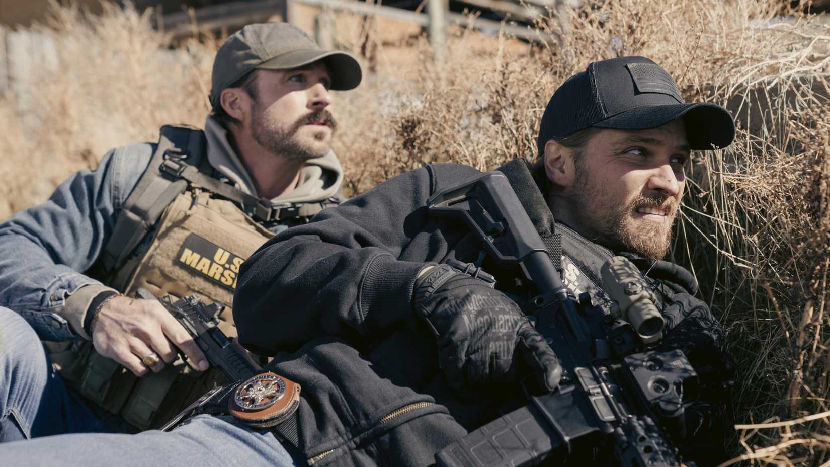 Luke Grimes as Kayce Dutton hiding behind bushes and holding a gun in Marshals season 1, episode 9