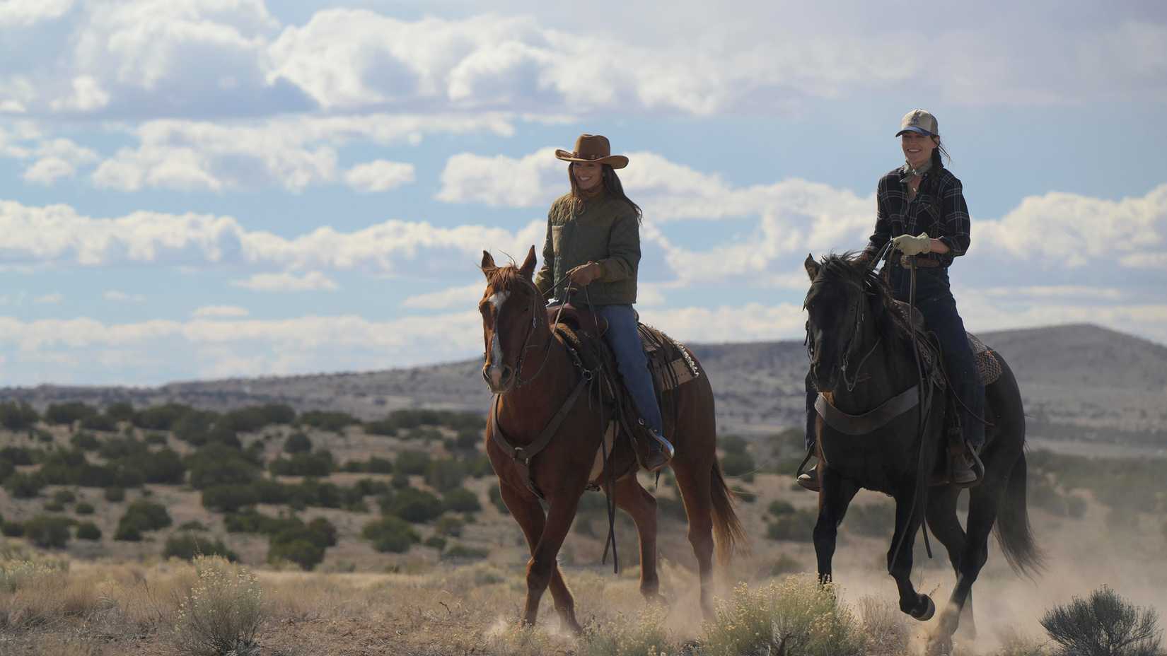 Ransom Canyon still featuring Minka Kelly as Quinn and Lauren Glazier as Angie O’Grady riding horses in front of a blue sky.