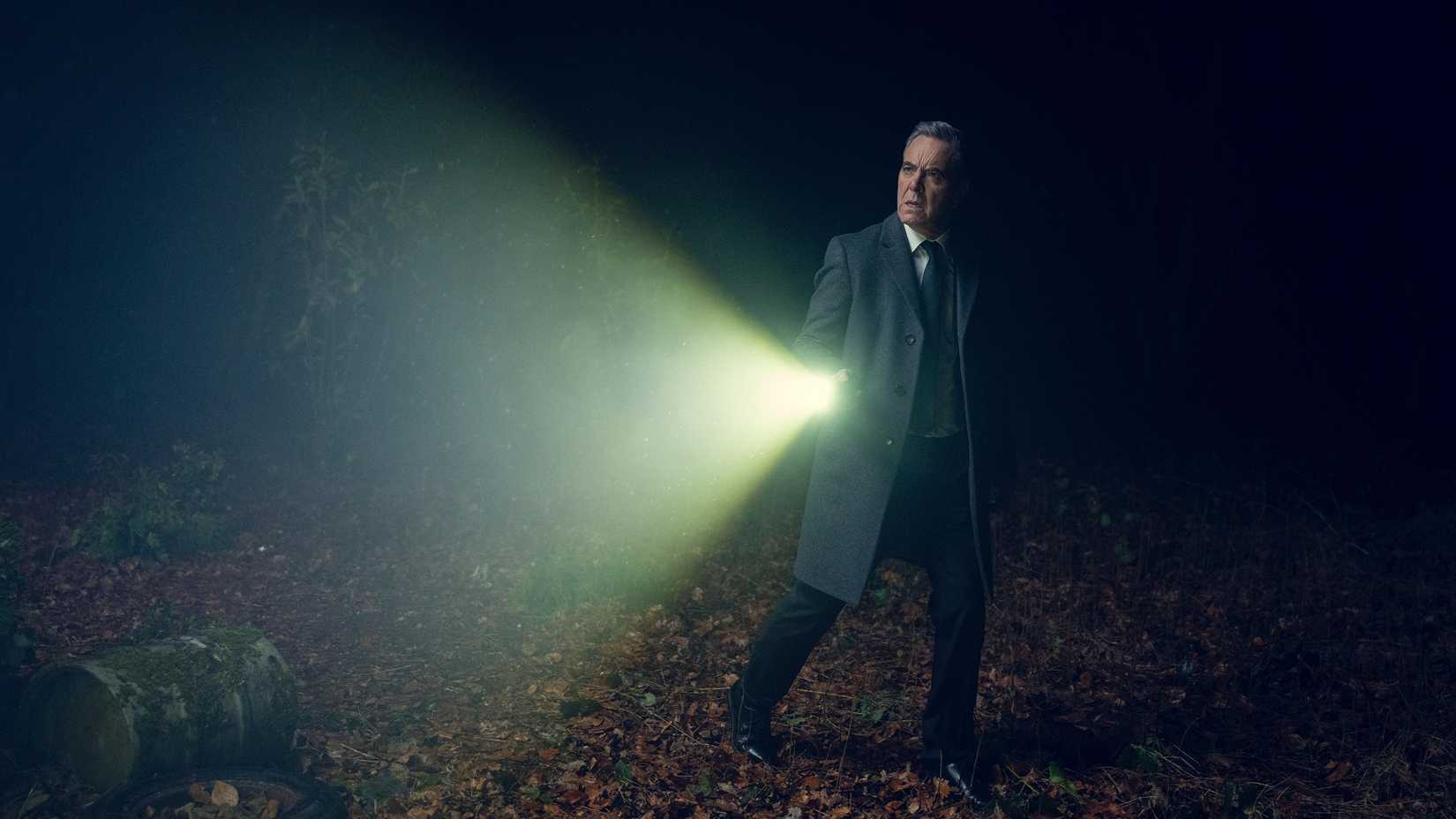 Harlan Coben's Run Away still featuring James Nesbitt in a jacket and tie, holding a flashlight in the woods.