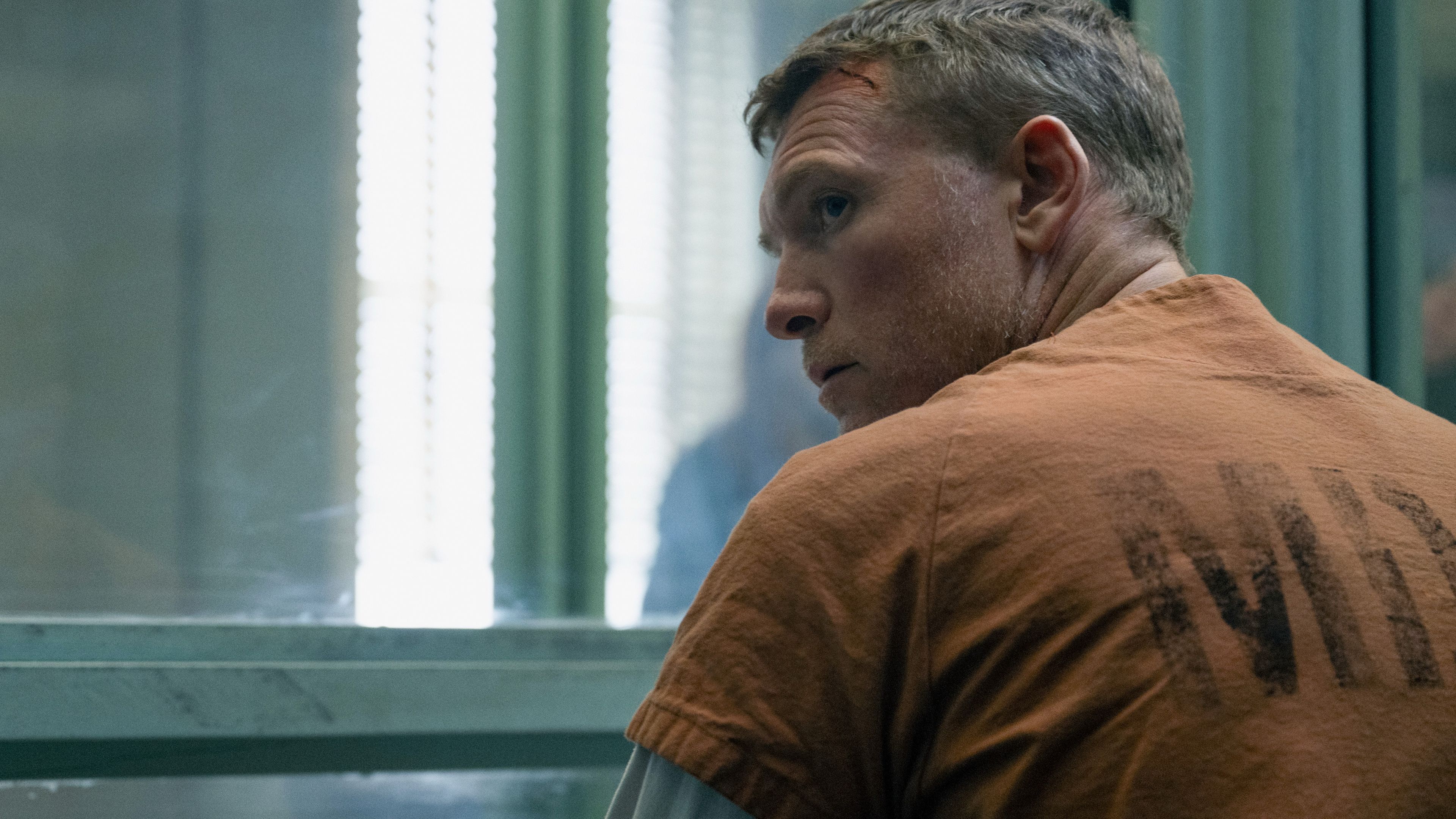 Sam Worthington's David looking suspiciously over his shoulder in a prison visitation window in I Will Find You