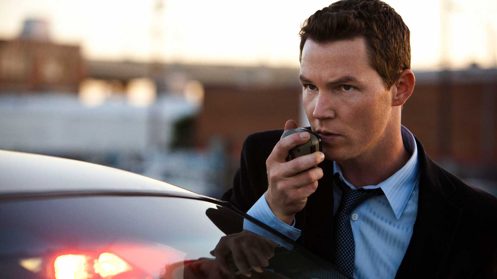 Shawn Hatosy speaking into a walkie while standing outside of his police car in Southland