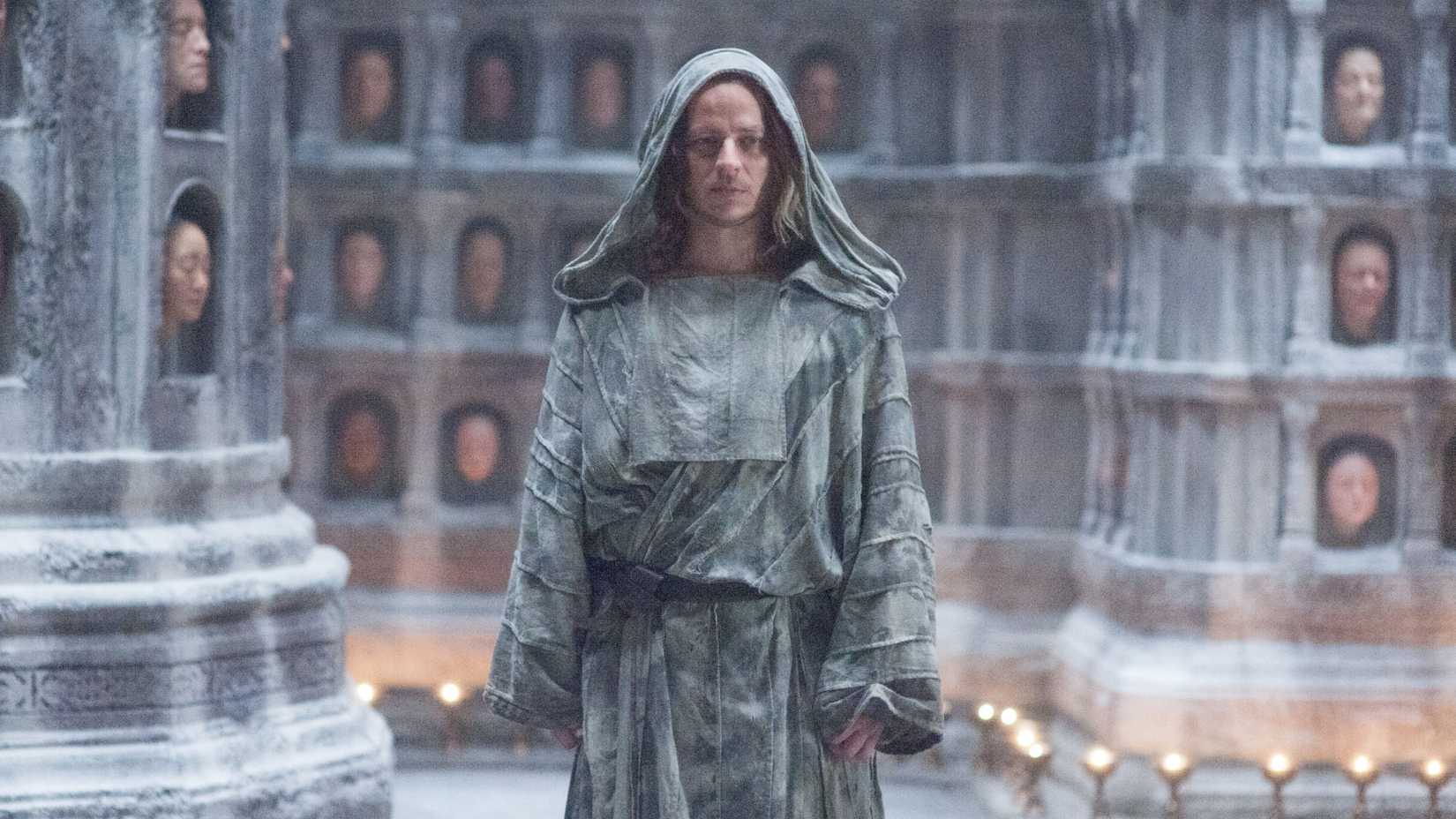 Jaqen H'ghar standing in front of a wall of faces