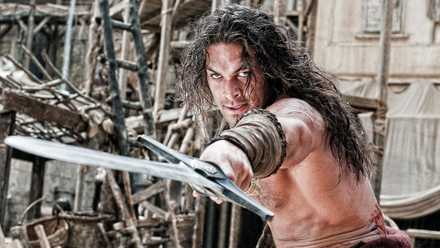 Jason Momoa as Conan the Barbarian, pointing a sword forward.