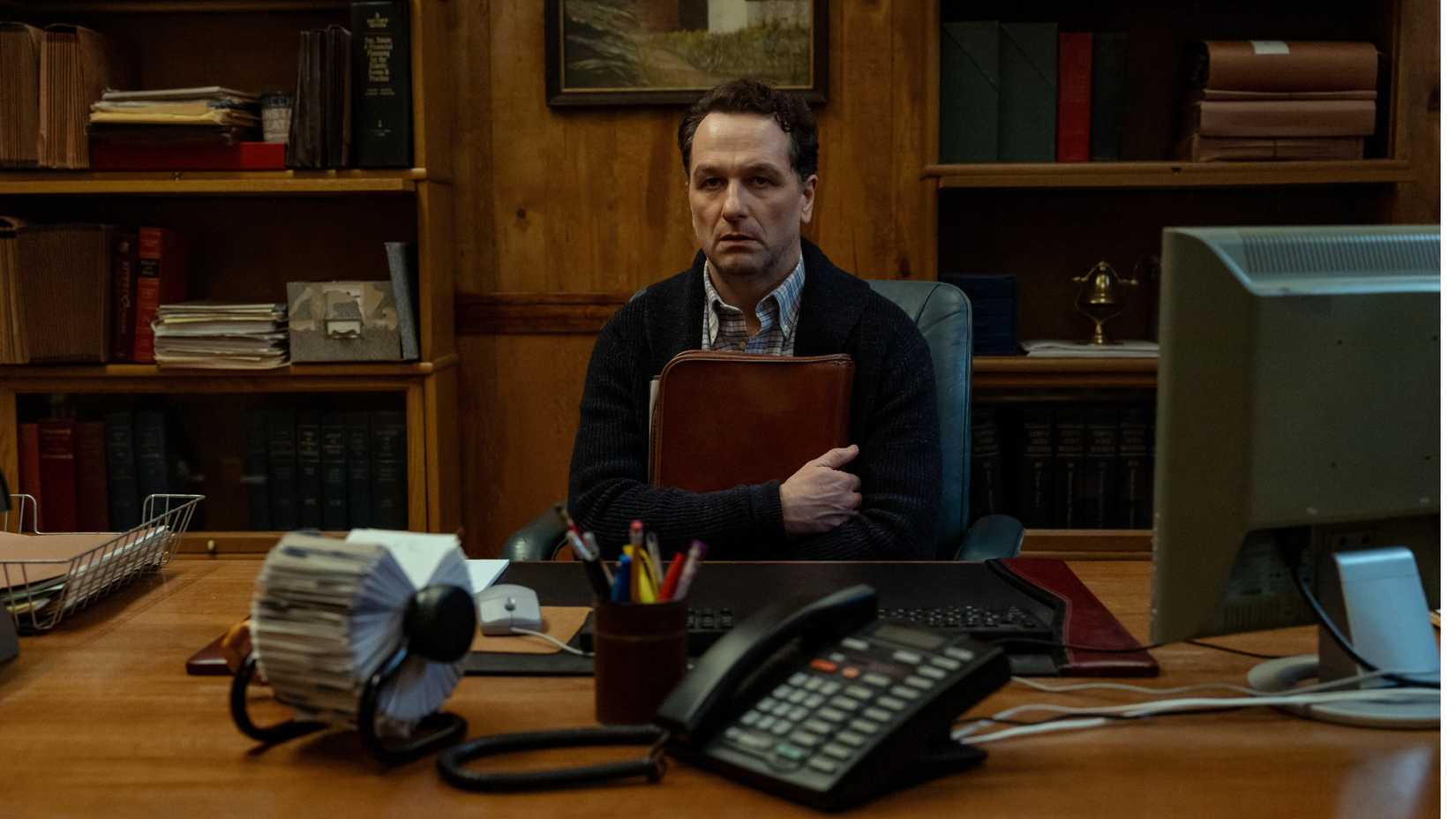 Widow's Bay still featuring Matthew Rhys as Mayor Tom Loftis, sitting behind his desk in fear.