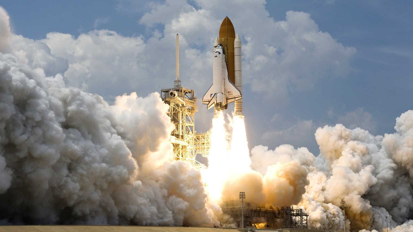 A rocket launches against a blue cloudy sky