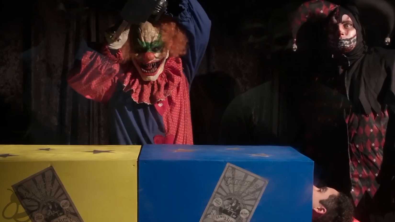 A clown with a chainsaw about to cut a box with a man inside in Circus Kane