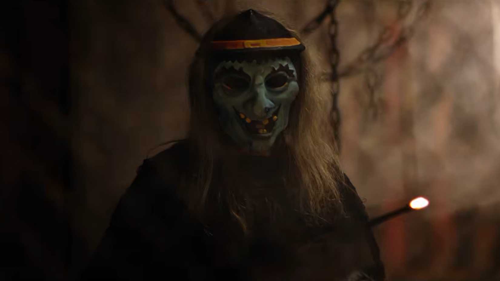 A figure in a witch mask holding a red hot poker in Haunt