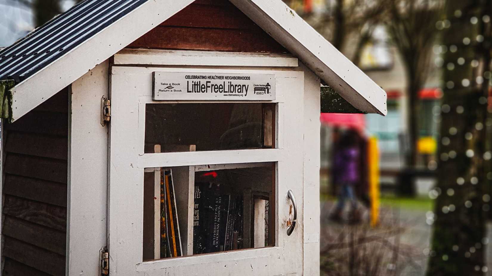 A white, house shaped Little Free Library has books inside