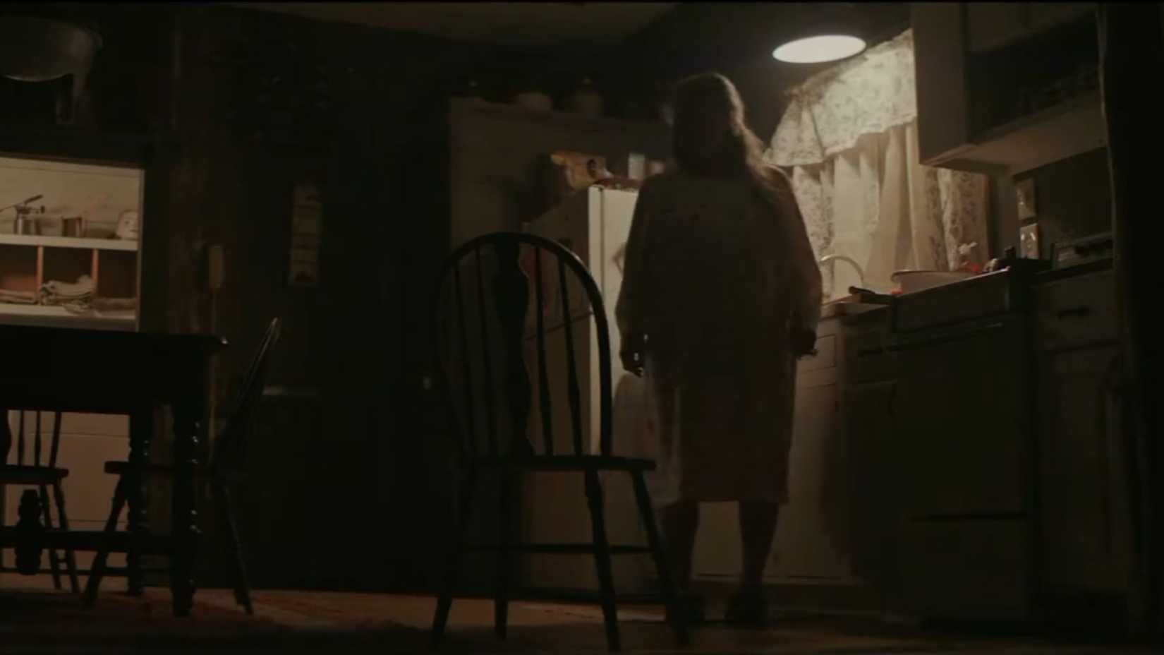 A woman in a dimly lit kitchen as a chair moves behind her in The Dark and the Wicked-1