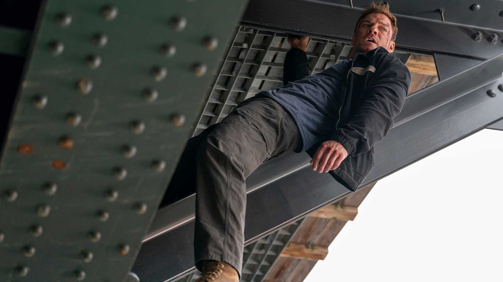 Alan Ritchson as Reacher hanging from a bridge in season 4