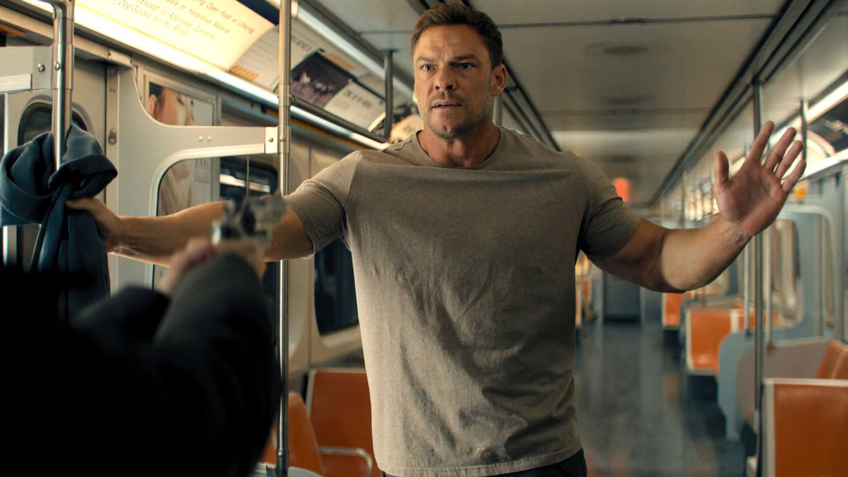 Alan Ritchson's Reacher holding his hands up while someone points a gun at him on the subway in Reacher season 4