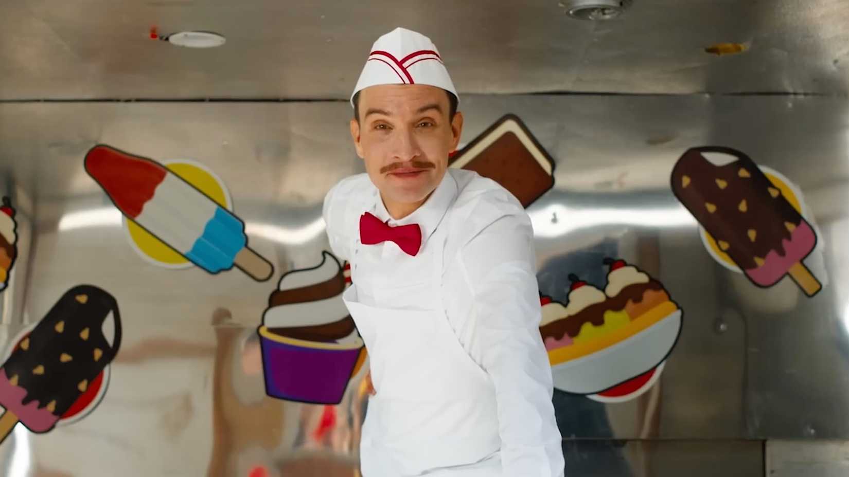 Ari Millen dressed as Ice Cream Man and smirking from his ice cream truck