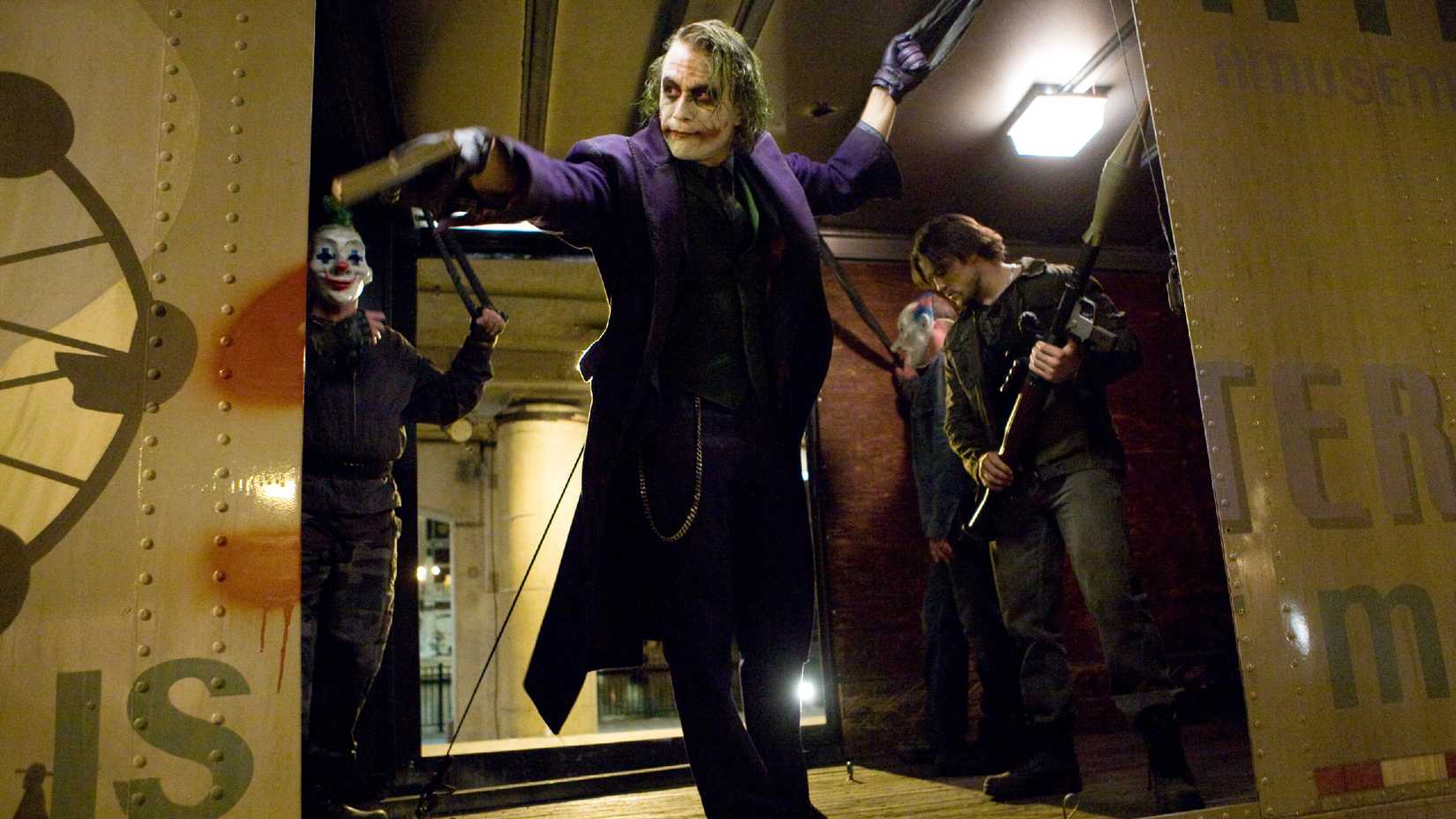 Heath Ledger as the Joker with pointing a gun out of the side of a truck in The Dark Knight