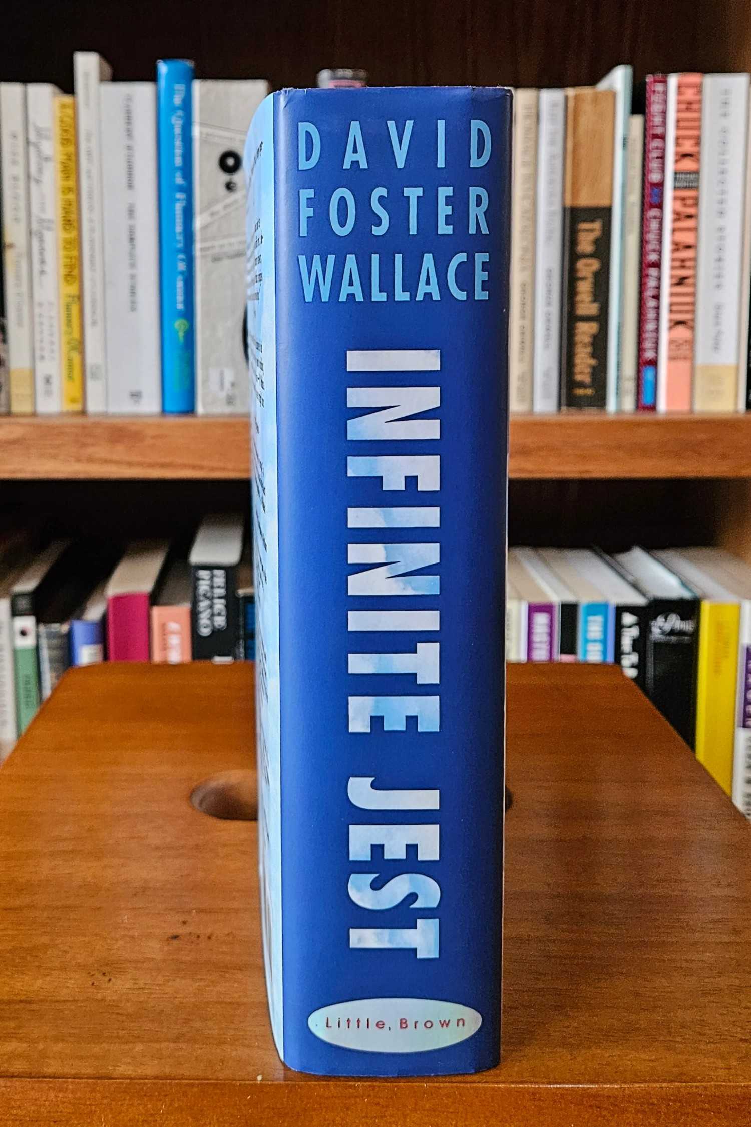 Infinite Jest hardcover standing up on a table in front of a bookshelf
