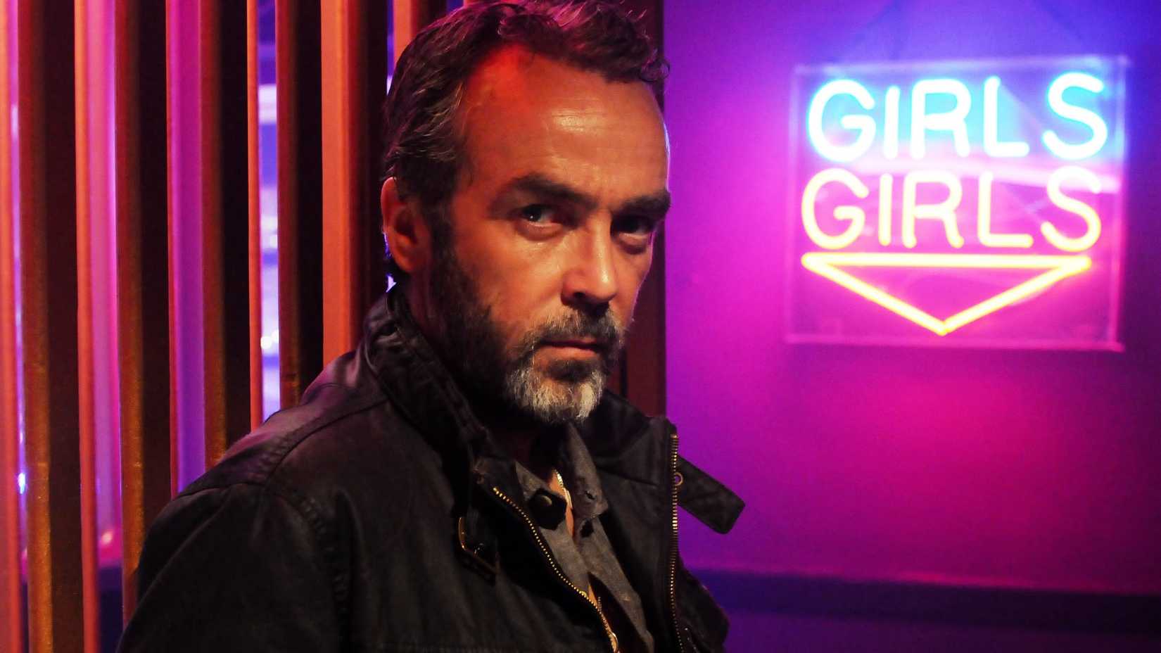 John Hanna in front of a neon sign in A Touch of Cloth